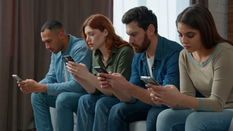 Group of people sitting in a row, focused on their smartphones, symbolizing how environmental misinformation spreads quickly through social media