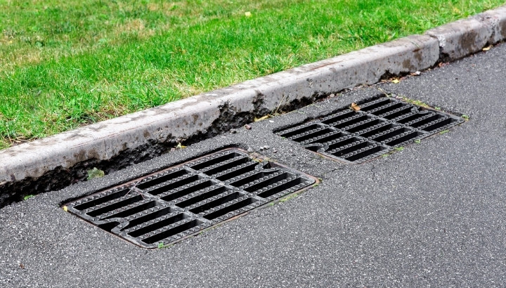 Two storm drain grates installed along an asphalt road beside a grassy area.